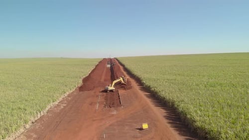 Excavator Digging Trench in Rural Field from Above