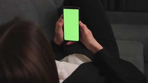 Closeup of Woman Lying on a Couch Using Smartphone with Green Mockup Screen