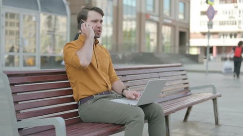 Man Using Laptop and Phone on Urban Bench