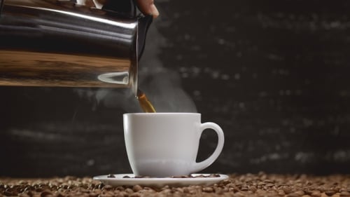 Coffee Being Poured into Cup Surrounded by Beans