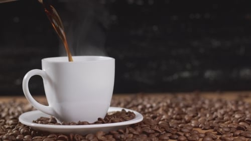 Steaming Coffee Poured into Mug on Coffee Beans