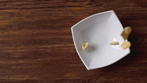 Corn Flakes Falling in White Bowl with Copyspace To the Left on Wooden Table