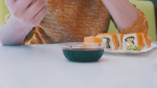 Frau mit Essstäbchen isst Sushi von einem Teller in einem japanischen Restaurant