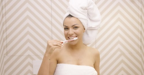 Woman Brushing Teeth in Bathroom with Towel