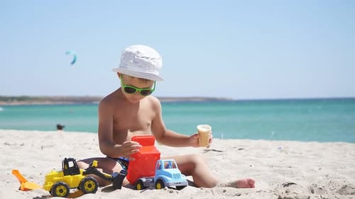 Sunny Summer Day, a Boy Plays with Sand and Toys, Cars on the Beach. a Child Eats Ice Cream While