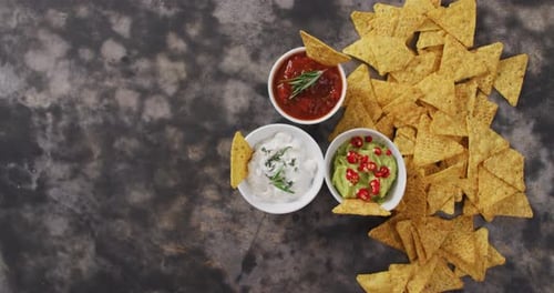 Primer plano de nachos y variedad de salsas sobre una superficie negra