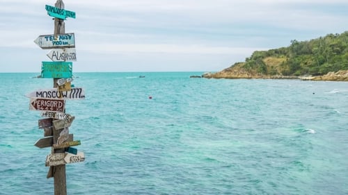 Wegweiser aus Holz am tropischen Felsstrand mit Meereswellen und Longtail-Boot