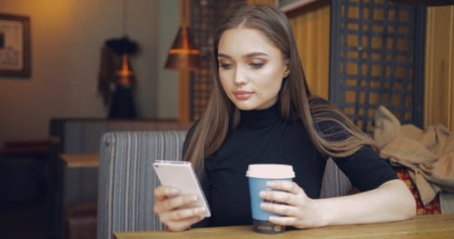 Young Woman Uses Smartphone at Cafe Table