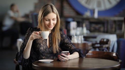 Stylishly Dressed Woman Drinks Coffee in a Small Restaurant, Sitting at a Wooden Table on Which
