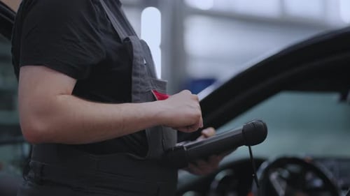 Ein Mechaniker in einer Nahaufnahme hält ein Tablet in den Händen und drückt auf den Bildschirm in der Nähe des Autos
