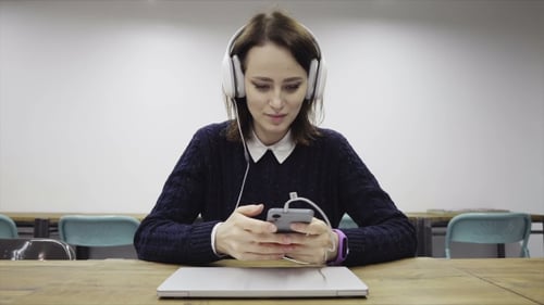 Young Happi Woman in Headphones Using a Smartphone in Office