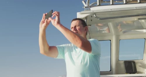 Side view of a Caucasian man on boat taking photos with his phone