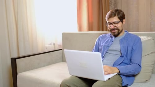 Man on Laptop Video Call, Relaxed on Sofa
