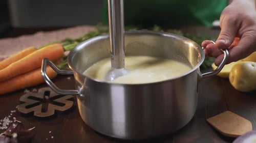 Le cuisinier utilise un mixeur plongeant pour faire de la purée de soupe dans la poêle en métal, cuire des aliments sains, de la purée