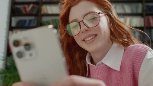 Attractive Student Woman Holding Modern Smartphone Texting Message in Home Office or Library