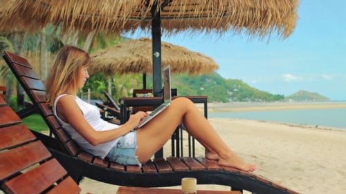 Jovem mulher freelancer sentada na espreguiçadeira com um laptop