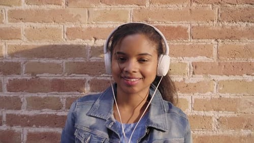 Woman with Headphones Smiling in Front of Brick Wall