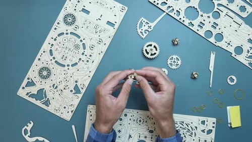 Man holding flywheel in hands, assembling wooden gear toy at home on table.