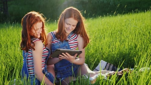 Teen Girls Using Tablet Together in Green Field
