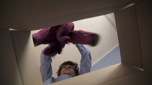 Man Unpacks Clothing from Inside Cardboard Box