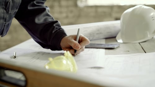 The Male Engineer Is Making Adjustments To the Construction Site Drawings, He Is in the Building of