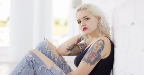 Tattooed Woman Leans Against Wall in Urban Setting