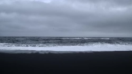 Crashing Waves on Black Sand Beach Under Cloudy Sky