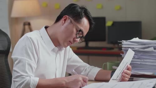 Close Up Of Asian Man Writing Something On Paper While Working With Documents At The Office