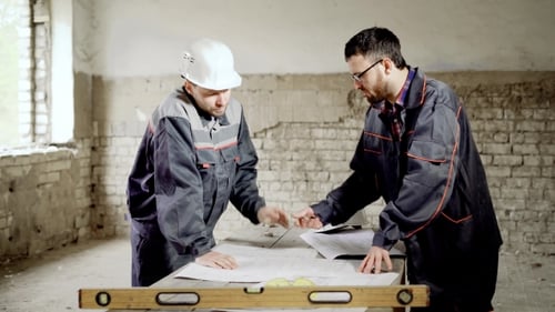 A Foreman and an Employee at the Building Construction Site. The Master Inspects the Drawing and