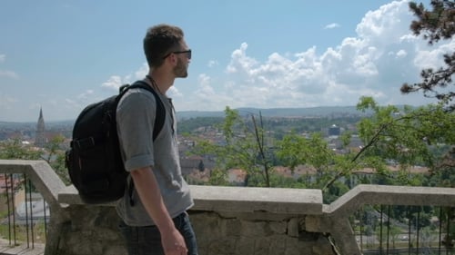 Man Traveler with Backpack Explores the City Looking at the Panoramic View of the City and the Coast