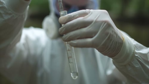 Person in Protective Suit Examining Liquid in Test Tube