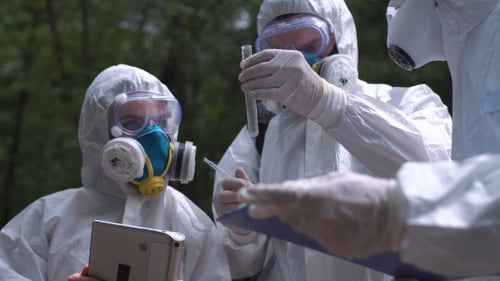 Scientists Examining Sample in Protective Suits Outdoors