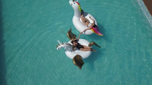 Aerial - Beautiful Girls in a Bikini on an Inflatable Pegasus and Unicorn Mattress in the Pool