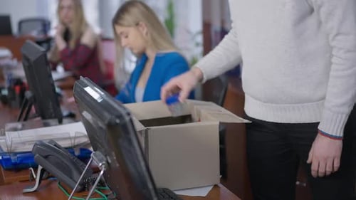 Unrecognizable Man Packing Cardboard Box in Office with Blurred Women Working at Background