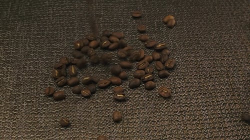 Coffee Beans Fall Next to Cup of Espresso