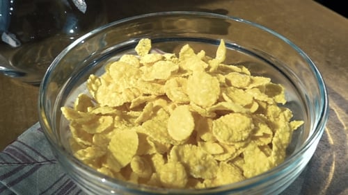 Corn Flakes Being Poured Into Clear Bowl
