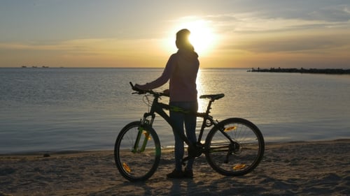 Lone Biker Stands on Beach at Sunrise