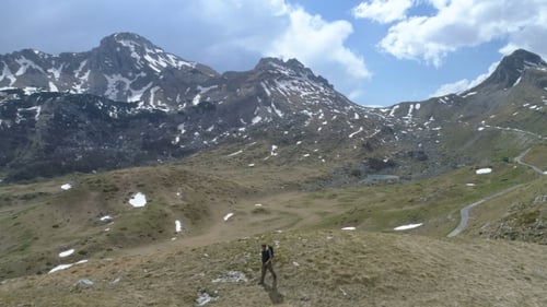 Hiker Walking Across Mountainous Terrain on Sunny Day