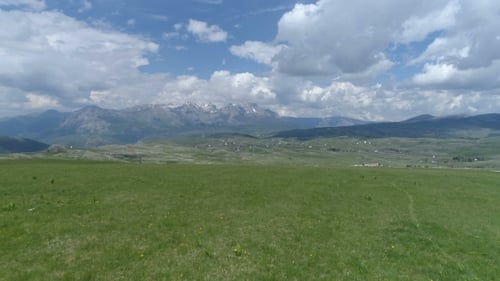Aerial Shot of Flying Over a Grassy Field in a Mountain Valley