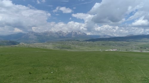 Aerial Shot of Flying Over a Grassy Field in a Mountain Valley