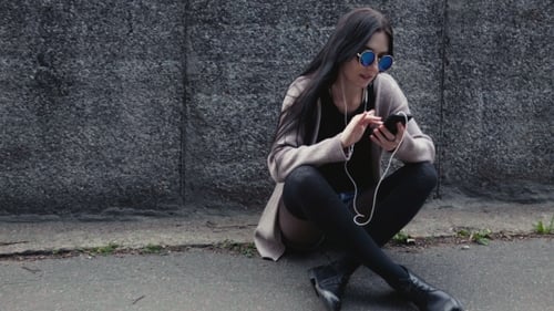 Woman Using Smartphone Sitting Against Urban Wall