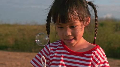 Cute little girl blowing soap bubbles in the summer park at sunset.