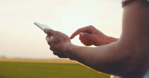Person using Cell Phone Against Rural Background at Sunset