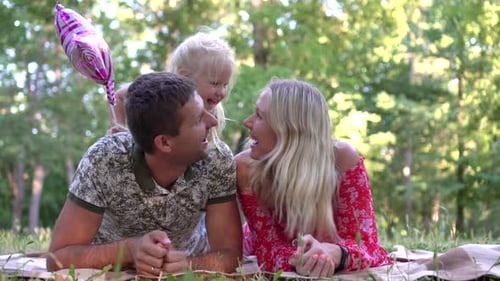 Happy Family with a Child in the Park Outdoors. Mom, Dad and the Child Relax on a Blanket in Nature.