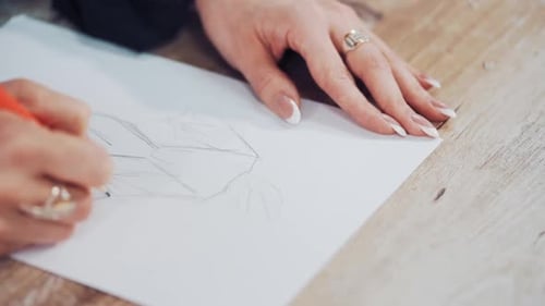 Young woman's hands of a fashion designer drawing sketches of clothes in the atelier.