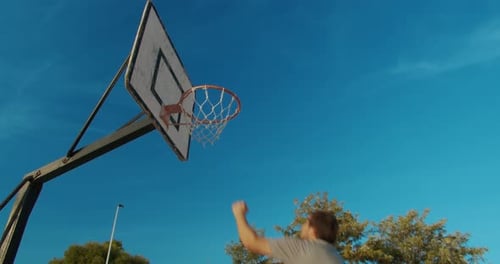 Männlicher Basketballspieler Slam Dunking auf einem Basketballplatz im Freien