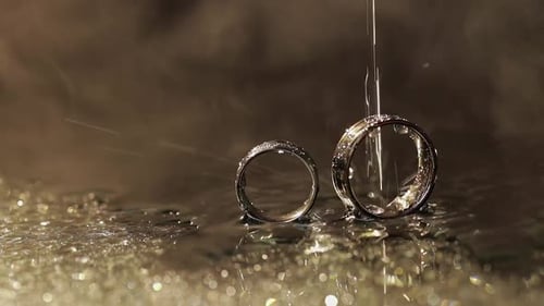 Wedding Rings on Dark Water Surface Shining with Light. Water Drops. Close Up