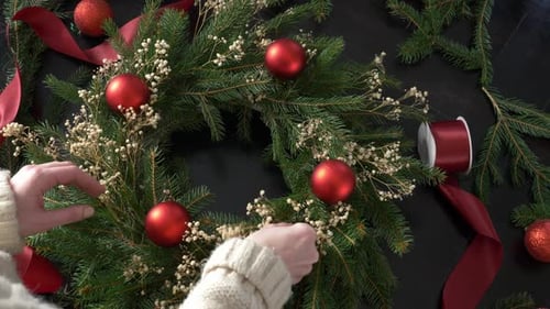 Woman Decorating a Christmas Wreath with Red Baubles