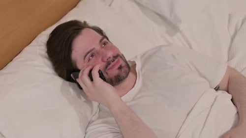 Man Relaxing in Bed Talking on Smartphone