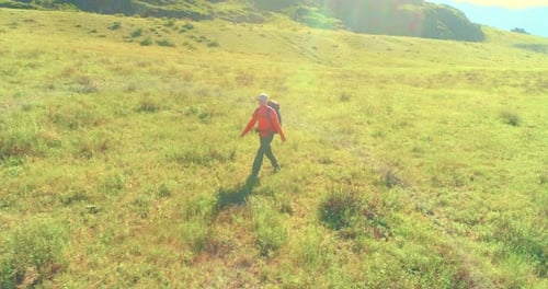 Flight Over Backpack Hiking Tourist Walking Across Green Mountain Field. Huge Rural Valley at Summer